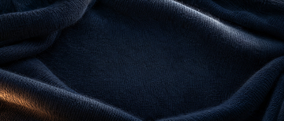 Close-up of a midnight blue brushed knit fabric in soft folds with a warm streak of lamplight